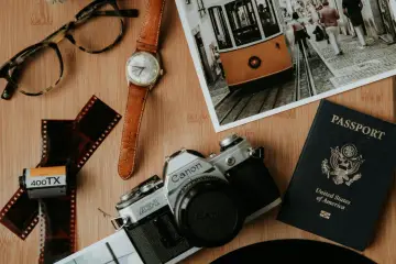 Paszport USA, aparat Canon, klisza, zegarek i okulary na drewnianym tle. Kto wydaje paszport? Rząd USA.
