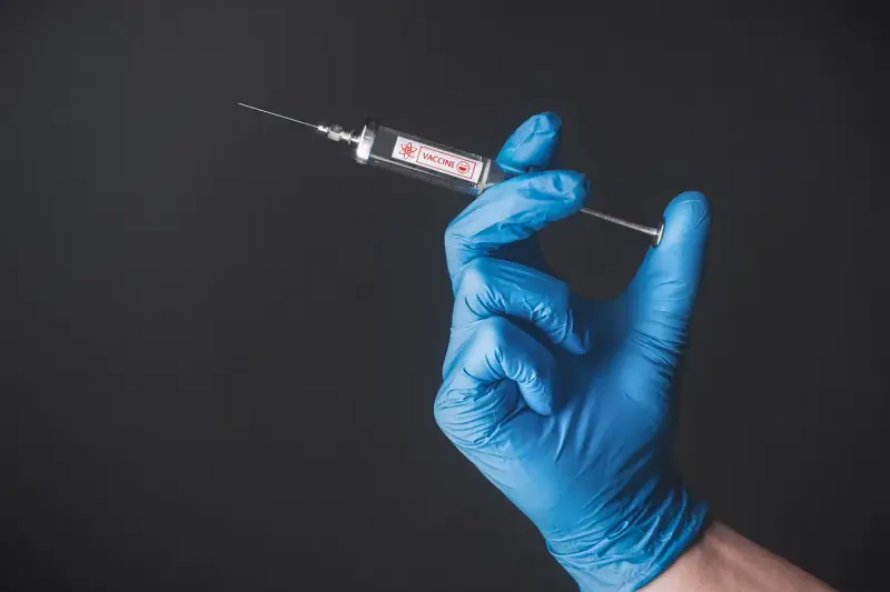Ręka w niebieskiej rękawiczce trzyma strzykawkę z napisem "VACCINE". To symbol nadziei na bezpieczne podróże, np. do Tunezji, gdzie tunezja szczepienia są kluczowe.