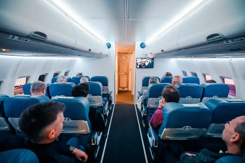 Wnętrze samolotu z pasażerami siedzącymi w rzędach. Wiele osób podróżuje, co potwierdza, że to najbezpieczniejszy środek transportu.