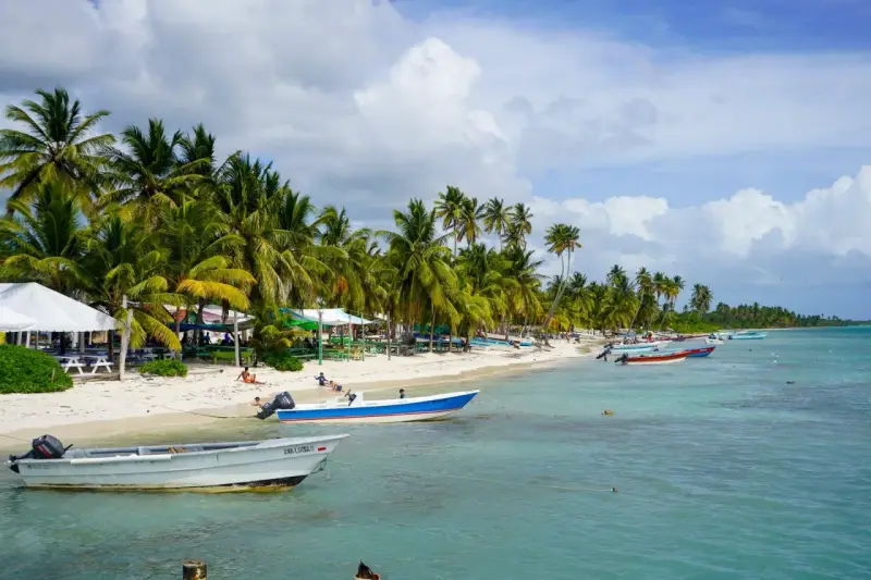 Rajski **Bavaro Beach** z palmami, białym piaskiem, turkusową wodą i łodziami.