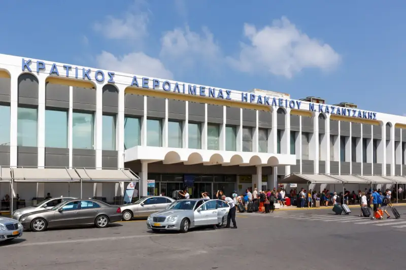 Lotnisko na Krecie, Heraklion N. Kazantzakis. Ludzie z bagażami czekają na transport przed nowoczesnym budynkiem terminalu.