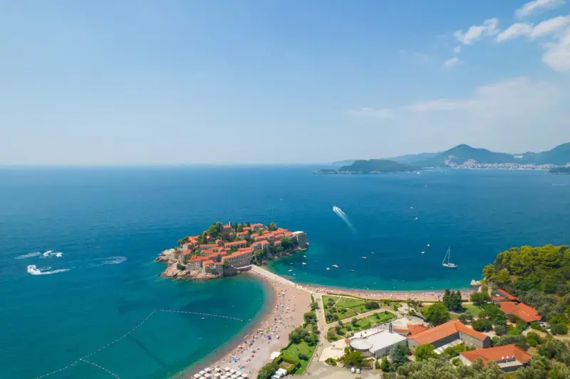 Sveti Stefan, perła Czarnogóry, idealne miejsce na wycieczki. Wyspa z czerwonymi dachami, plaża, turkusowe morze i góry w tle.